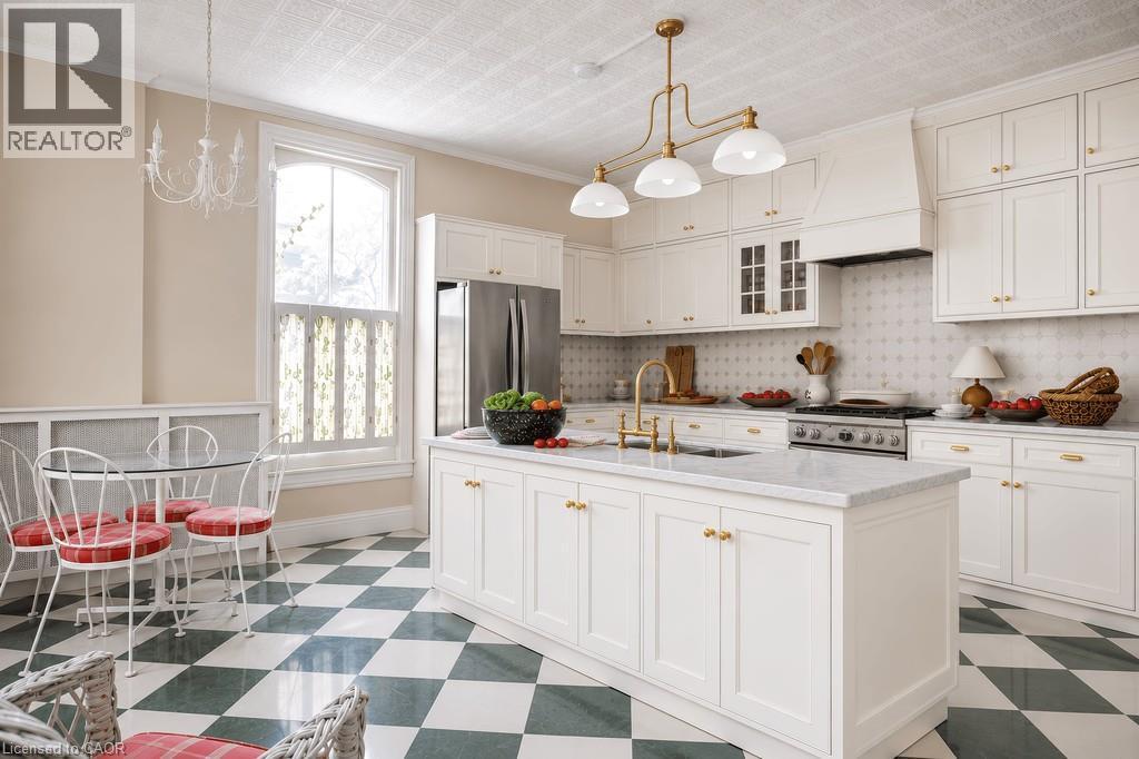 Spacious kitchen featuring an expansive center island with an undermount sink, white shaker cabinetry, stainless steel appliances, and a checkered floor - 370 Hess Street S, Hamilton, ON - Indoor Photo Showing Kitchen
