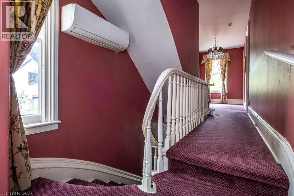 Staircase featuring a white wooden balustrade and a wall-mounted air conditioning unit - 370 Hess Street S, Hamilton, ON - Indoor Photo Showing Other Room
