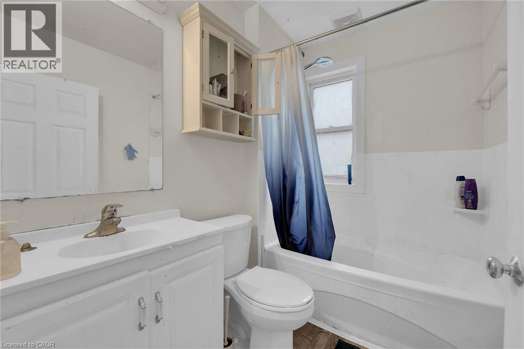 Full bathroom featuring a white vanity with integrated sink, coordinating wall-mounted storage cabinet, and a bathtub with an overhead shower and window - 738 King Street W, Hamilton, ON - Indoor Photo Showing Bathroom