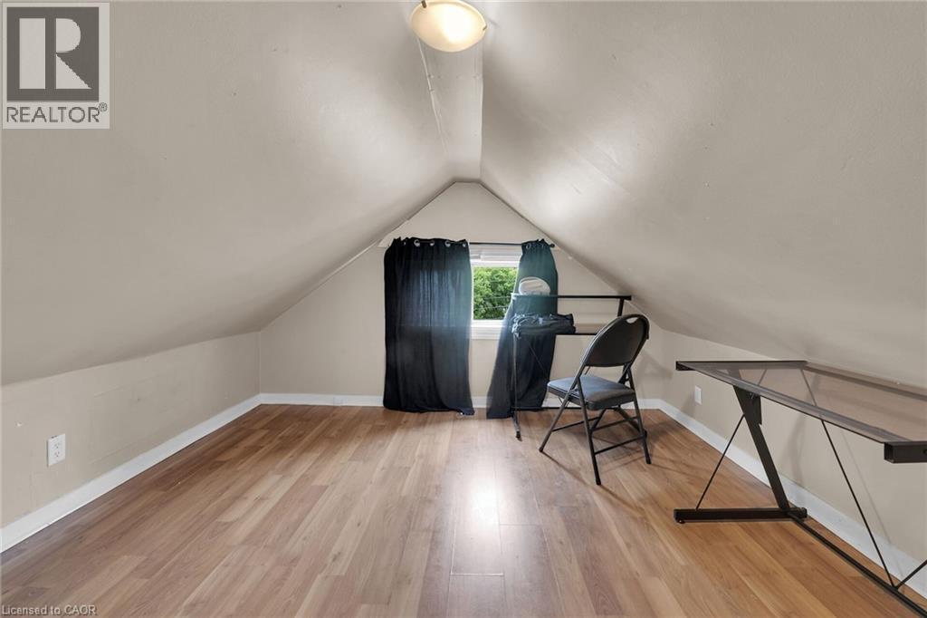 Attic space featuring wood-finish flooring, an angled ceiling, and a prominent window - 738 King Street W, Hamilton, ON - Indoor Photo Showing Other Room
