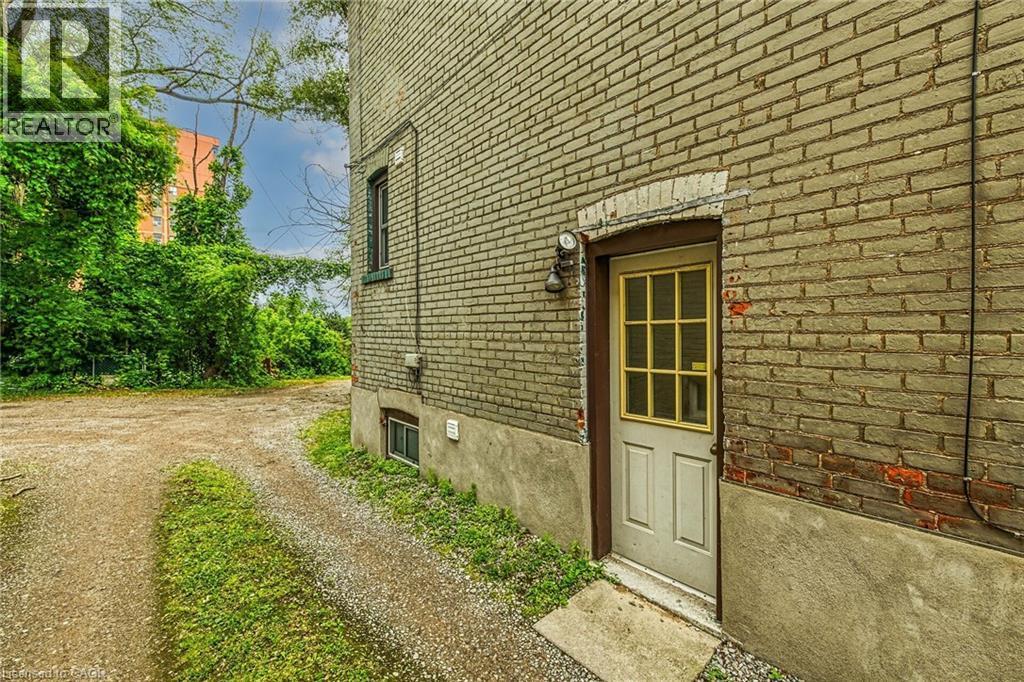 Brick exterior featuring a basement entry door with windowpanes and an exterior light fixture - 738 King Street W, Hamilton, ON - Outdoor