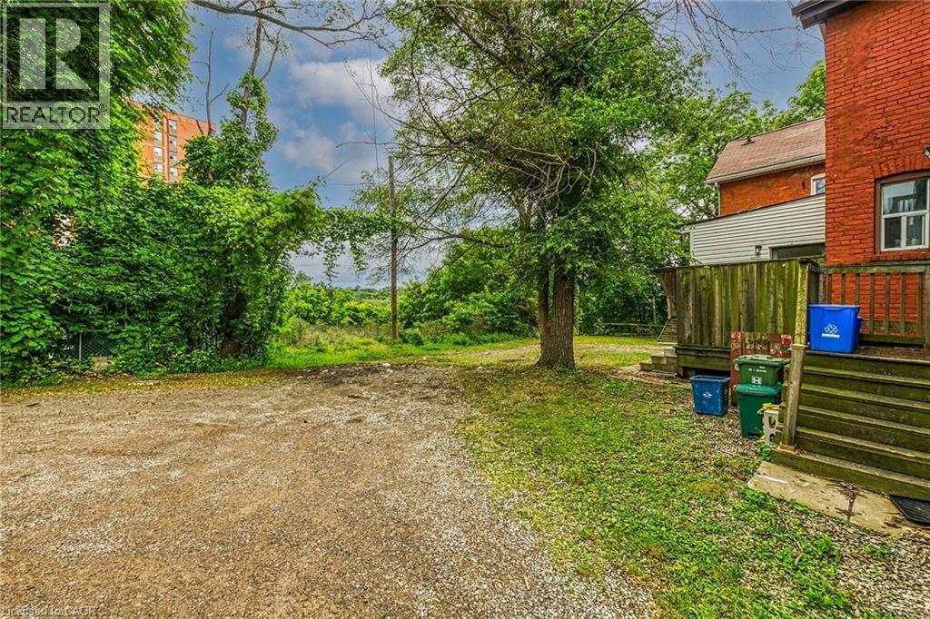Gravel parking area bordered by mature trees and lush green foliage - 738 King Street W, Hamilton, ON - Outdoor