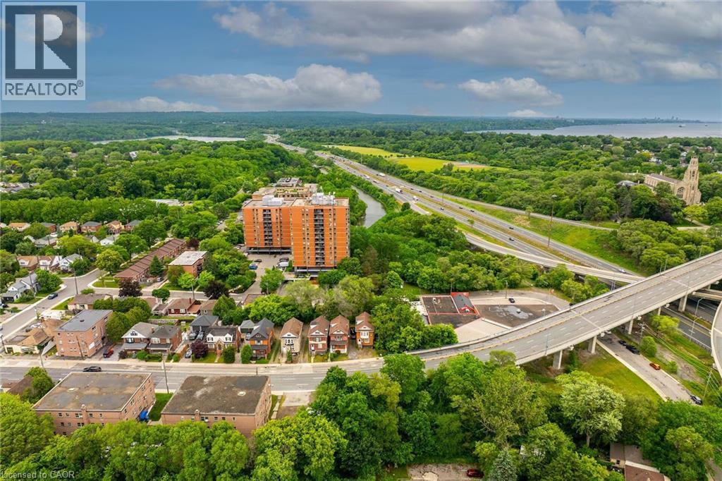 Aerial perspective showcasing a multi-lane highway system, surrounding green spaces, and a residential area with a prominent high-rise building - 738 King Street W, Hamilton, ON - Outdoor With View