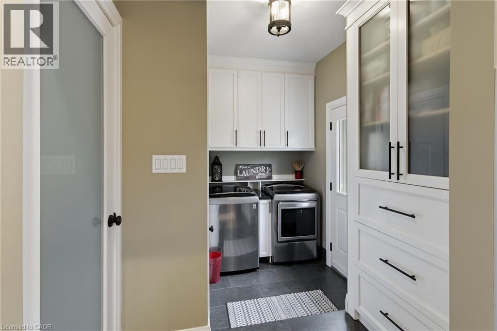 Dedicated laundry area featuring white cabinetry, dark hardware, stainless steel appliances, dark tile flooring, and a frosted glass door - 2116 Binbrook Road E, Hamilton, ON - Indoor