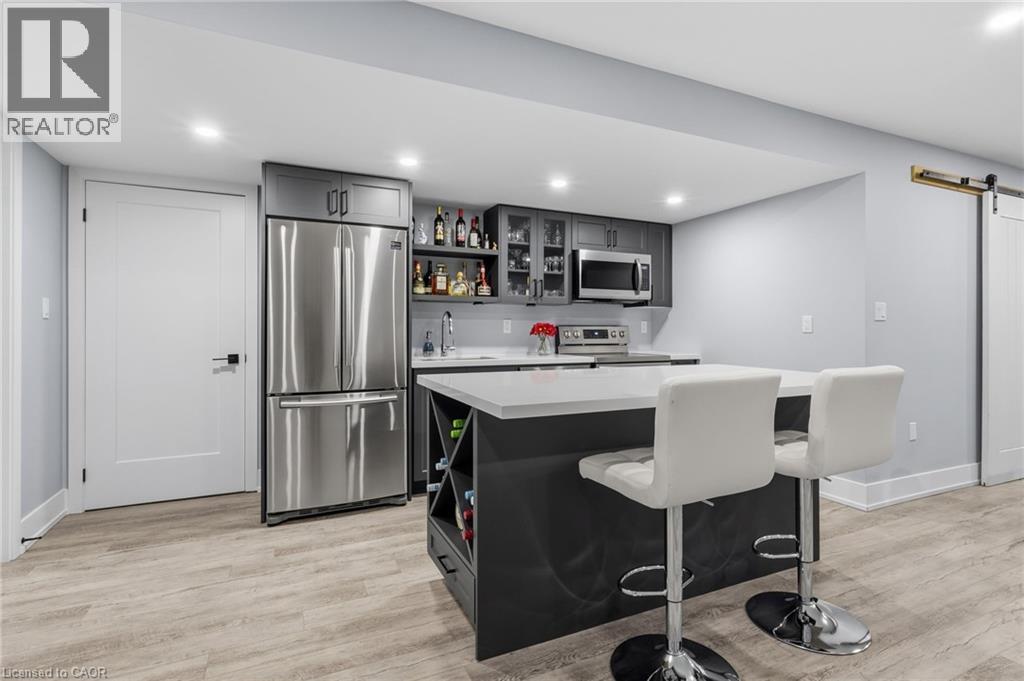 Contemporary kitchenette featuring a large stainless steel refrigerator, built-in microwave, and ample gray cabinetry with glass-front accents - 2116 Binbrook Road E, Hamilton, ON - Indoor Photo Showing Kitchen