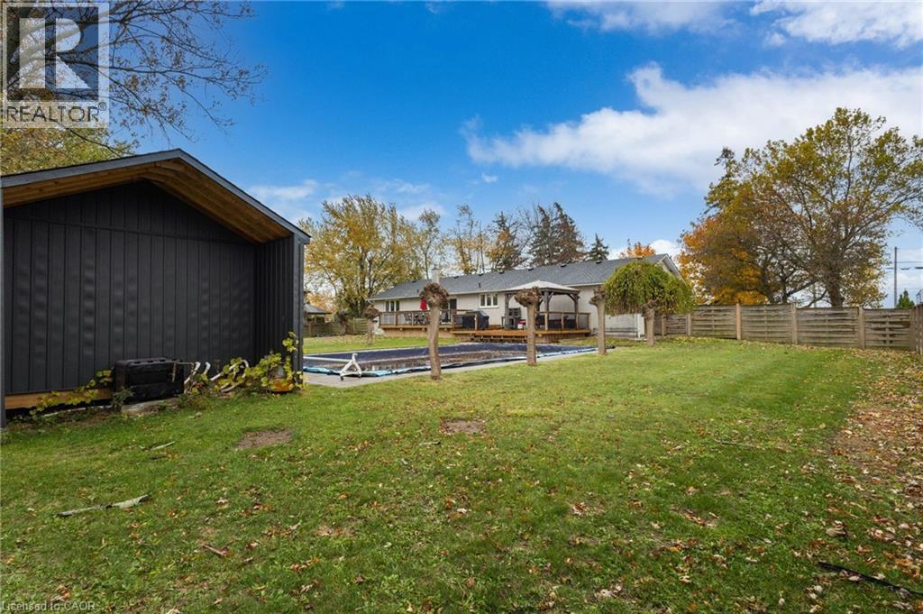 Expansive backyard featuring a covered pool, detached storage shed with dark vertical siding, a wooden privacy fence, and mature trees - 2116 Binbrook Road E, Hamilton, ON - Outdoor With Deck Patio Veranda