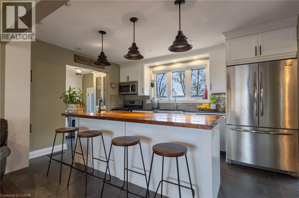 Kitchen featuring a central island with a wood-finish countertop, white cabinetry, stainless steel appliances, a tile backsplash, and dark tile flooring - 2116 Binbrook Road E, Hamilton, ON - Indoor Photo Showing Kitchen