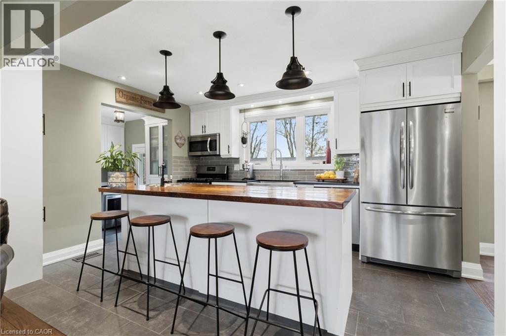 Kitchen featuring a wood-finish peninsula with seating, stainless steel appliances, white cabinetry, and a subway tile backsplash - 2116 Binbrook Road E, Hamilton, ON - Indoor Photo Showing Kitchen With Upgraded Kitchen