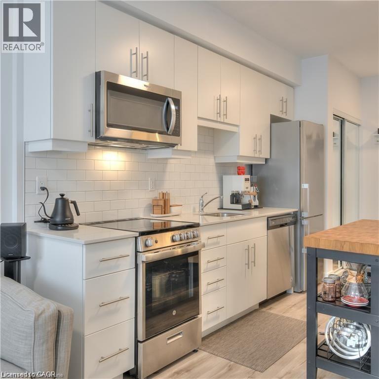 Contemporary kitchen featuring white cabinetry, stainless steel appliances, light-toned countertops, subway tile backsplash, Pictured island not included. An island will be in place for new tenant. - 247 Northfield Drive E Unit# 207, Waterloo, ON - Indoor Photo Showing Kitchen With Stainless Steel Kitchen With Upgraded Kitchen