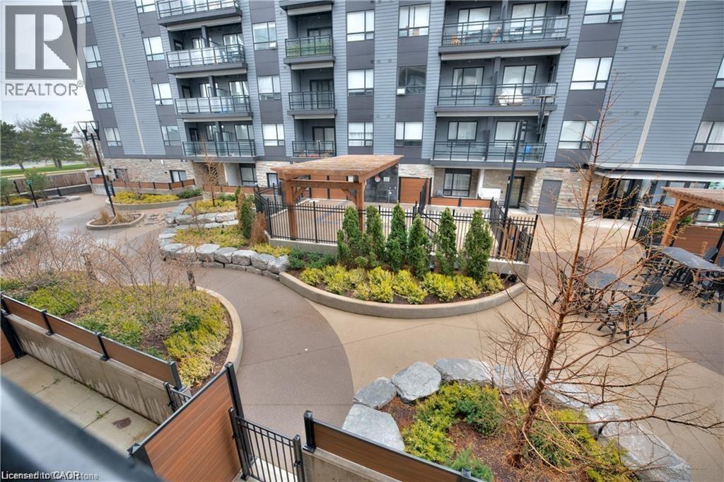 Expansive courtyard featuring a winding concrete pathway, multiple pergolas, and decorative landscaping with various plantings and stone elements - 247 Northfield Drive E Unit# 207, Waterloo, ON - Outdoor With Balcony
