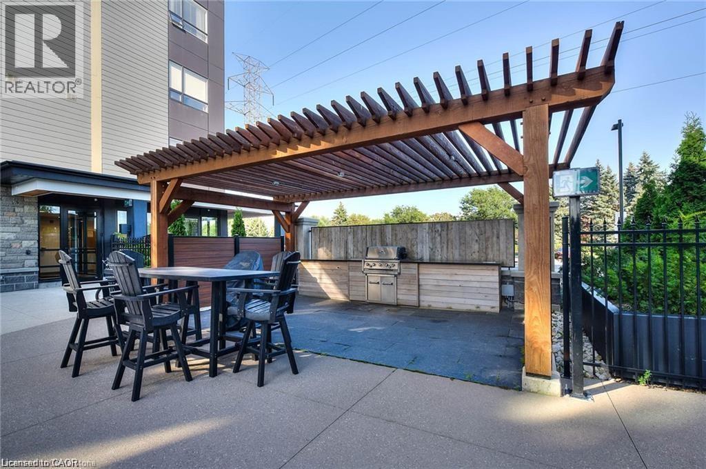 Outdoor entertainment area featuring a substantial wood pergola, integrated barbecue station, and concrete patio flooring - 247 Northfield Drive E Unit# 207, Waterloo, ON - Outdoor With Exterior