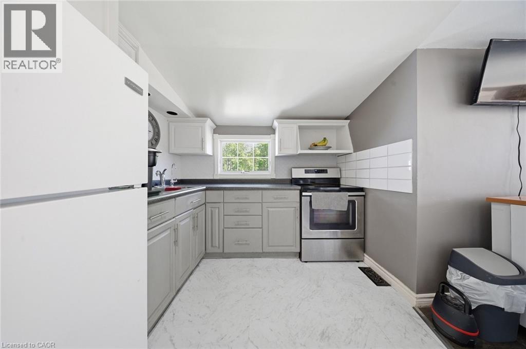 Kitchen featuring light gray cabinetry, dark countertops, a stainless steel range, white subway tile backsplash, and a window providing natural light - 401 West Street, Simcoe, ON - Indoor Photo Showing Kitchen
