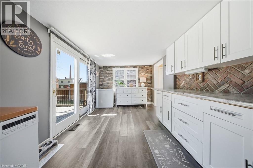 Modern kitchen featuring white shaker cabinetry with brushed nickel hardware, a brick-patterned backsplash, and wood-finish flooring - 401 West Street, Simcoe, ON - Indoor Photo Showing Kitchen