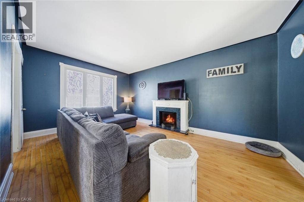Living area featuring hardwood flooring, a white mantel fireplace with a dark surround, white baseboards, and a three-panel window with patterned privacy film - 401 West Street, Simcoe, ON - Indoor Photo Showing Living Room With Fireplace
