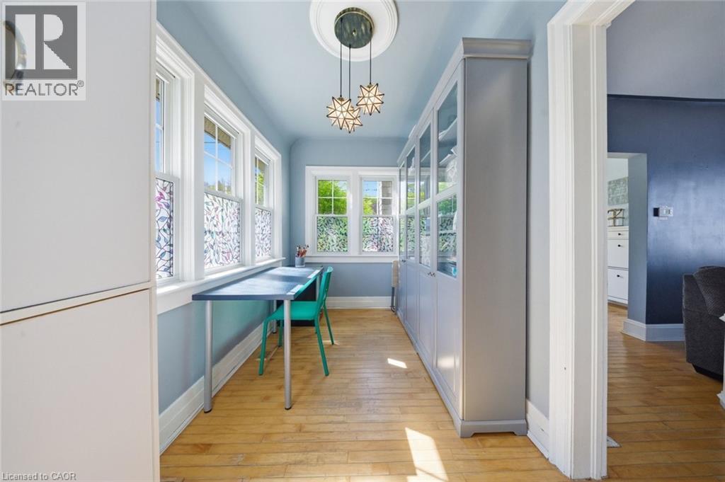 Dedicated workspace featuring expansive windows, built-in cabinetry with glass panels, wood-finish flooring, a decorative ceiling medallion, and contemporary pendant lighting - 401 West Street, Simcoe, ON - Indoor Photo Showing Other Room