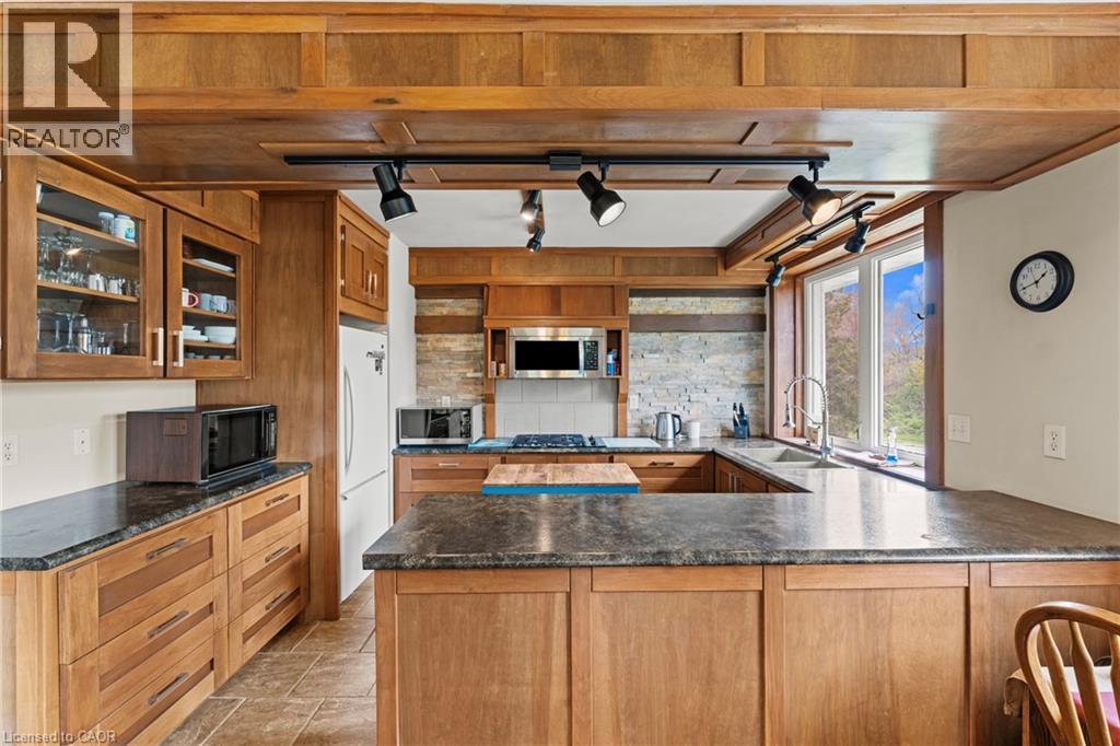 Kitchen featuring a U-shaped countertop layout with dark stone-finish surfaces, extensive wood cabinetry, and a stone tile backsplash - 3 San Pedro Drive, Hamilton, ON - Indoor Photo Showing Kitchen