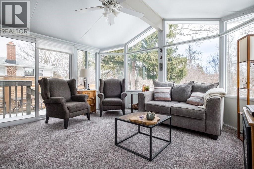 Sunroom featuring an angular wall of windows, a vaulted ceiling with a ceiling fan, plush gray carpeting, and a sliding glass door providing exterior access - 19 Chateau Court, Hamilton, ON - Indoor Photo Showing Living Room