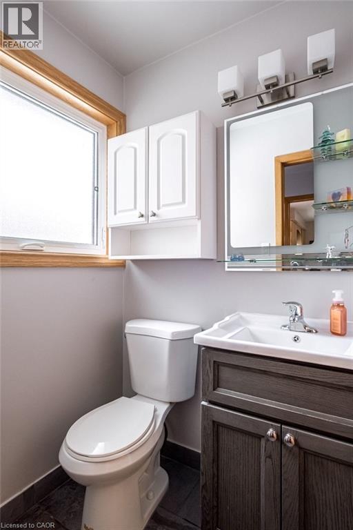 Bathroom with a window featuring wood trim, a white vanity with an integrated sink, a wall-mounted mirror, and overhead lighting - 19 Chateau Court, Hamilton, ON - Indoor Photo Showing Bathroom