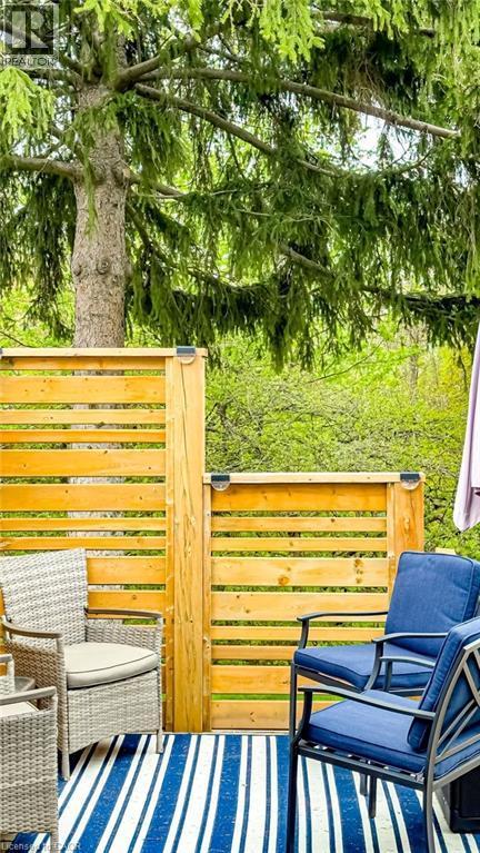 Outdoor patio area featuring a slatted wooden privacy screen with integrated lighting, a striped area rug, and mature trees providing natural canopy - 19 Chateau Court, Hamilton, ON - Outdoor With Deck Patio Veranda