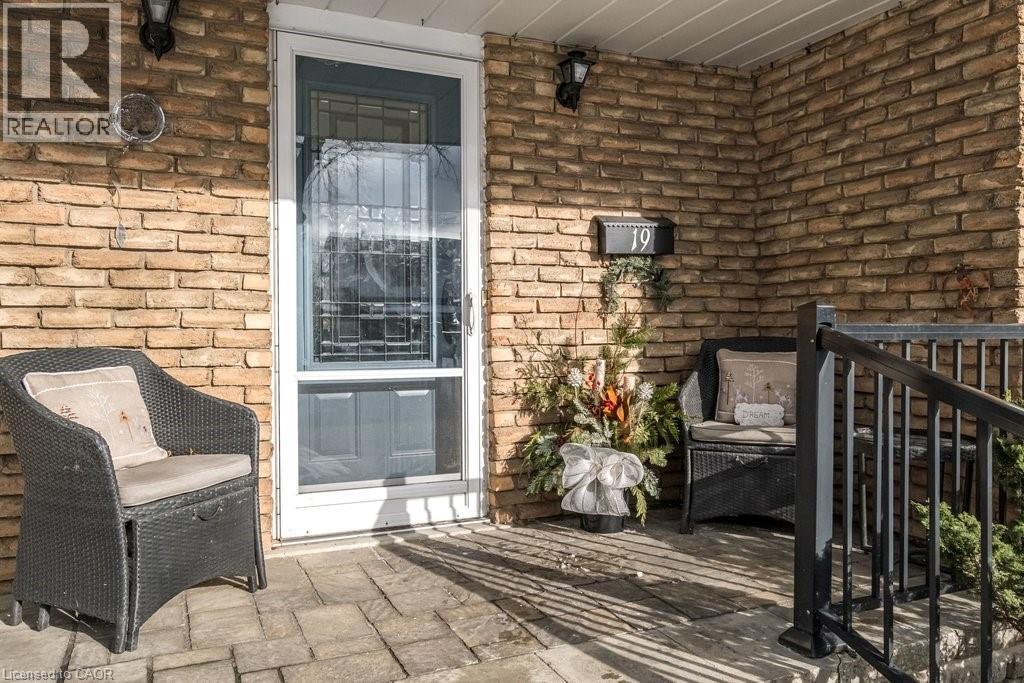 Inviting brick exterior porch with paver flooring, featuring a storm door with decorative grille, and a black metal handrail - 19 Chateau Court, Hamilton, ON - Outdoor With Deck Patio Veranda With Exterior