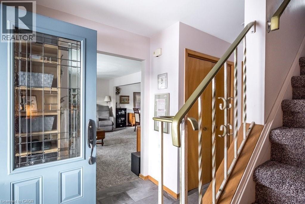 Entryway featuring a blue paneled door with decorative glass, tiled flooring, and a carpeted staircase with a brass-toned metal railing - 19 Chateau Court, Hamilton, ON - Indoor Photo Showing Other Room