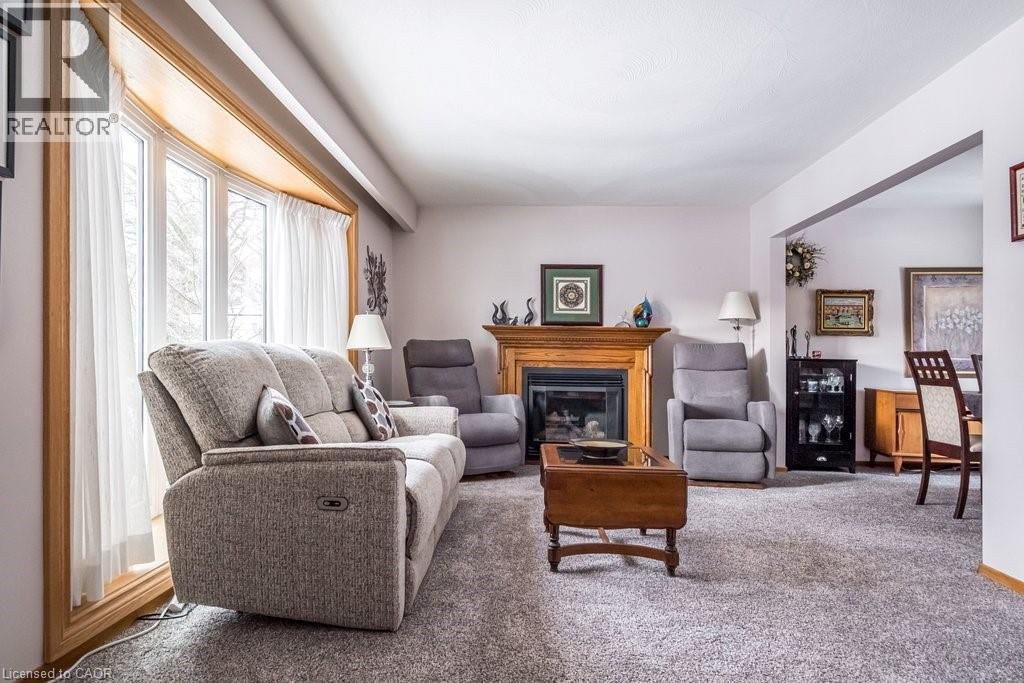 Living area featuring a bay window with wood trim, wood-surround fireplace, and light-colored carpet flooring - 19 Chateau Court, Hamilton, ON - Indoor Photo Showing Living Room With Fireplace