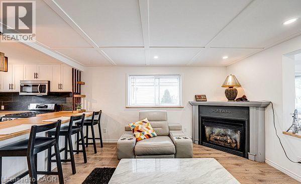 Living area featuring a corner fireplace with a decorative mantel, wood-finish flooring, and recessed lighting - 43 Adair Avenue S, Hamilton, ON - Indoor Photo Showing Living Room With Fireplace