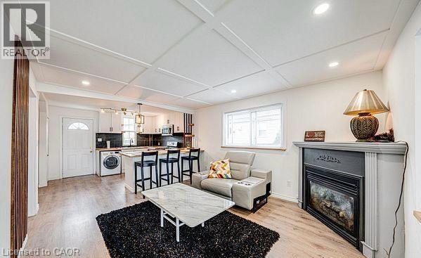 Open-concept living space featuring wood-finish flooring, a coffered ceiling with recessed lighting, and a built-in fireplace with a mantel - 43 Adair Avenue S, Hamilton, ON - Indoor Photo Showing Living Room With Fireplace