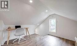 Attic space featuring sloped ceilings, recessed lighting, wood-finish flooring, a single window, and white trim -