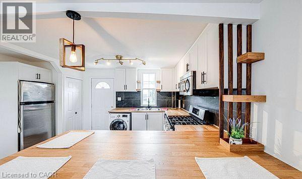 Kitchen featuring wood-finish countertops, white cabinetry with dark hardware, stainless steel appliances, and a black tile backsplash - 43 Adair Avenue S, Hamilton, ON - Indoor