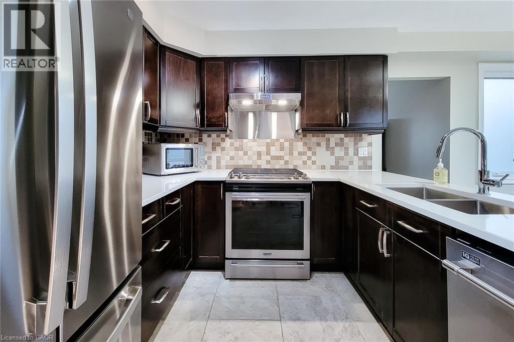 Kitchen featuring dark wood cabinetry, white countertops, stainless steel appliances, a mosaic tile backsplash, and light-toned tile flooring - 49 Ashwood Drive, Cambridge, ON - Indoor Photo Showing Kitchen With Stainless Steel Kitchen With Double Sink With Upgraded Kitchen