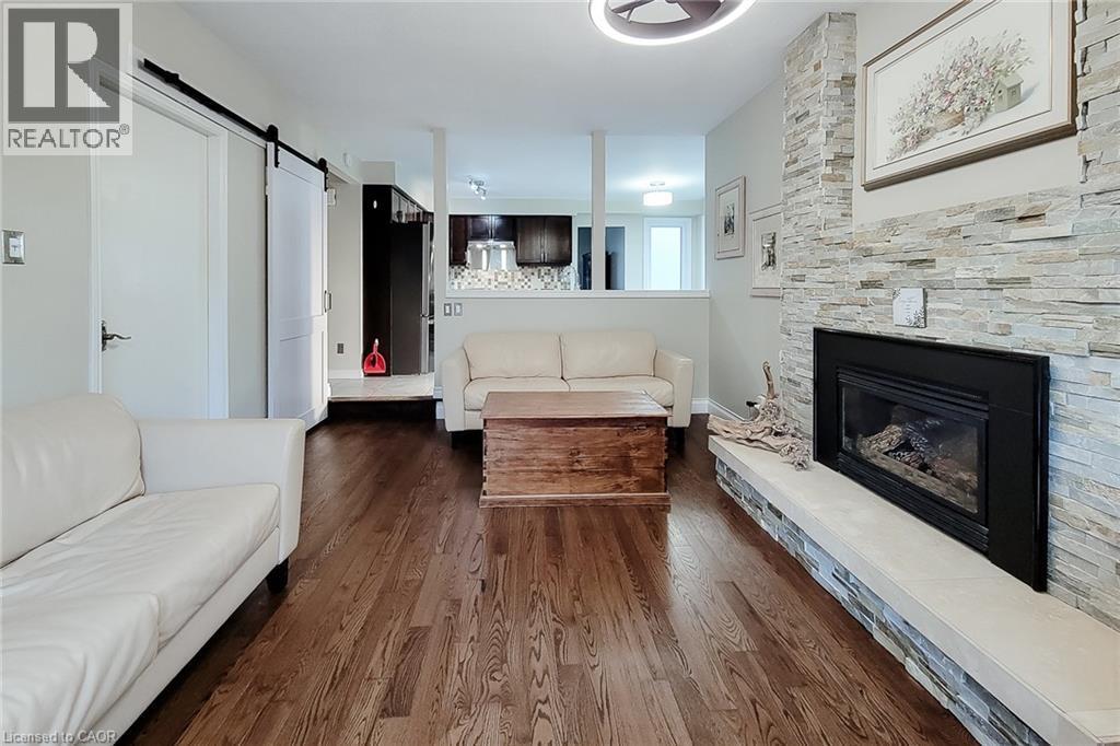 Living area featuring wood-finish flooring, a stacked stone fireplace with hearth, and a contemporary ceiling fixture - 49 Ashwood Drive, Cambridge, ON - Indoor Photo Showing Living Room With Fireplace