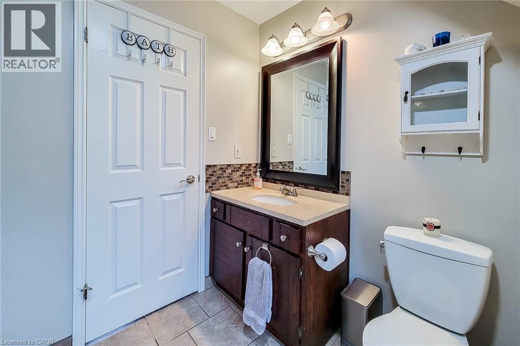 Bathroom featuring a dark wood-finish vanity with a light-toned countertop, a rectangular mirror, a three-light vanity fixture, and a mosaic tile backsplash - 49 Ashwood Drive, Cambridge, ON - Indoor Photo Showing Bathroom