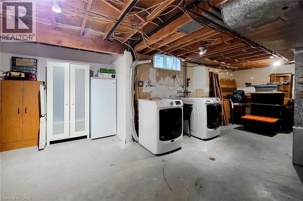 Basement laundry area featuring two front-loading machines, exposed ceiling joists, concrete flooring, and a small window - 49 Ashwood Drive, Cambridge, ON - Indoor Photo Showing Laundry Room