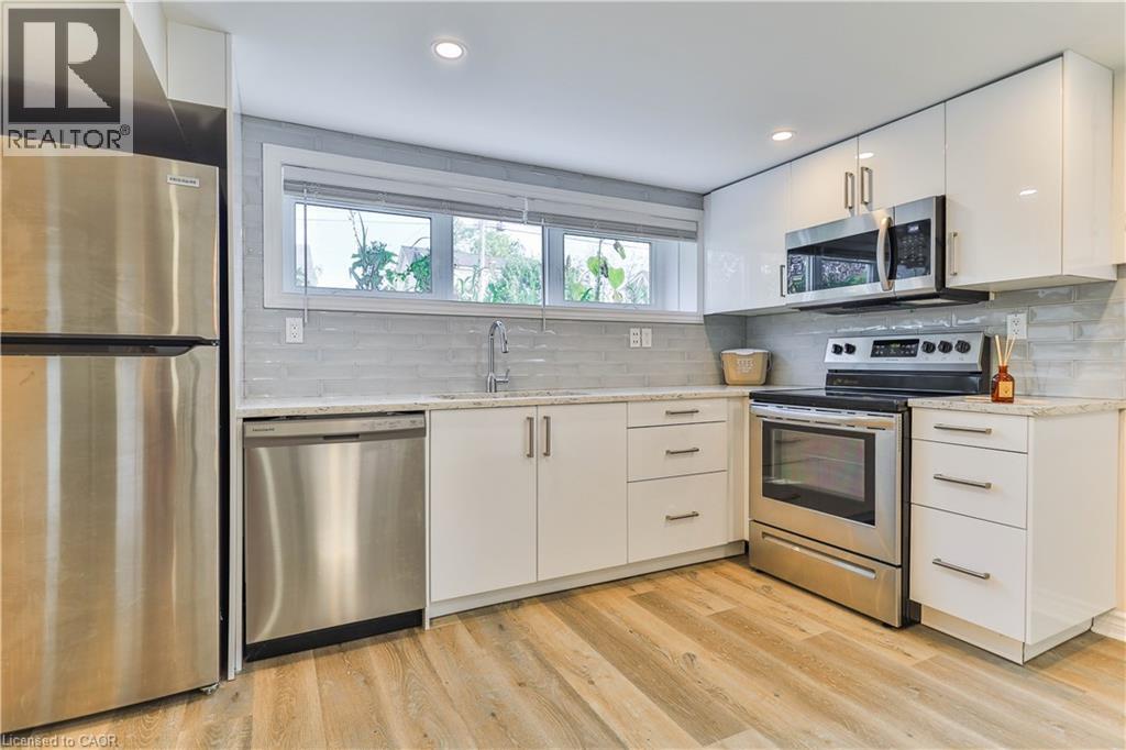 Kitchen featuring stainless steel appliances, white flat-panel cabinetry, light-toned countertops, a horizontal tile backsplash, and wood-finish flooring - 38 Dunkirk Drive Unit# B, Hamilton, ON - Indoor Photo Showing Kitchen With Stainless Steel Kitchen With Upgraded Kitchen