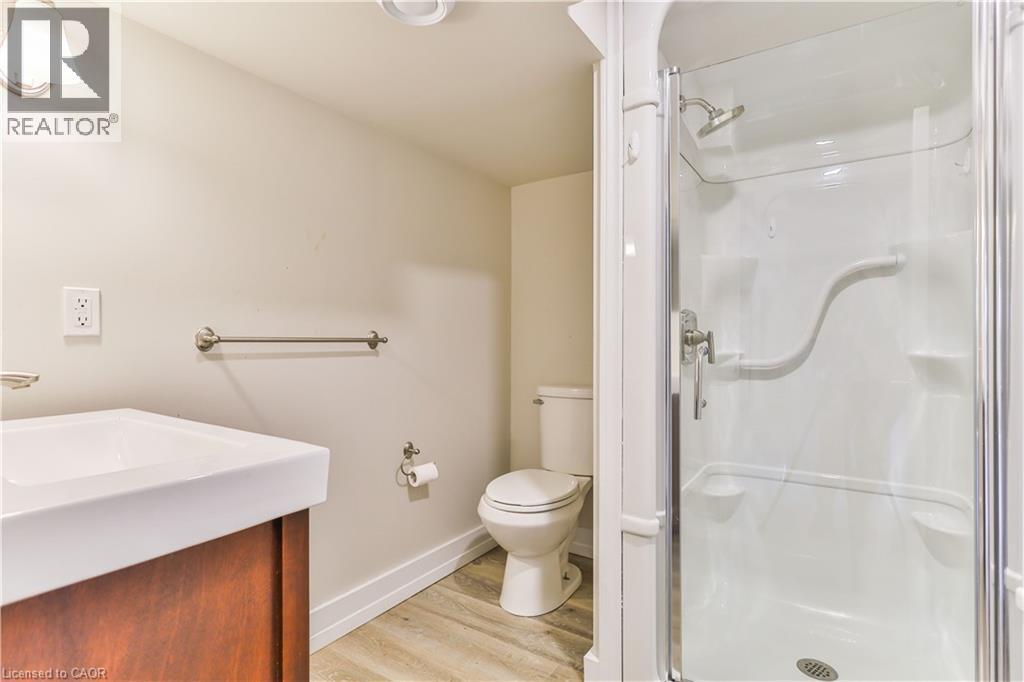 Compact bathroom featuring a glass-enclosed shower, single vanity with integrated sink, wood-finish cabinetry, and neutral wall tones - 38 Dunkirk Drive Unit# B, Hamilton, ON - Indoor Photo Showing Bathroom