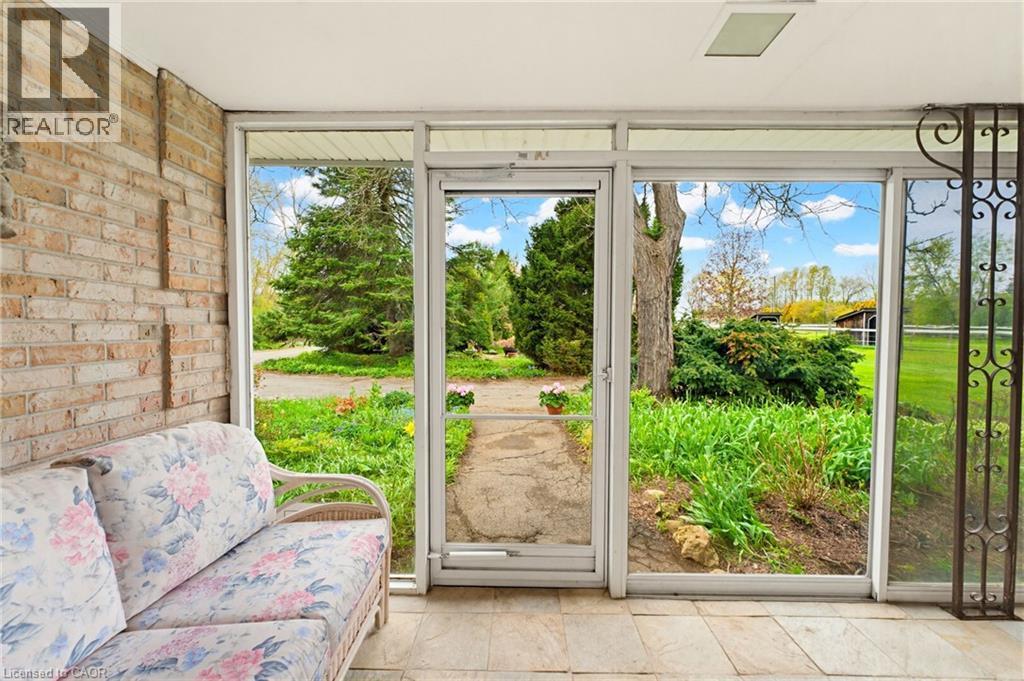 Enclosed porch featuring a brick wall, tiled flooring, expansive windows, and a glass door opening to a landscaped outdoor area - 10 Huisman Lane, Hamilton, ON