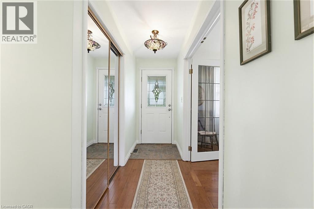 Entryway featuring wood-finish flooring, a decorative overhead light fixture, and a white door with a leaded glass insert - 10 Huisman Lane, Hamilton, ON