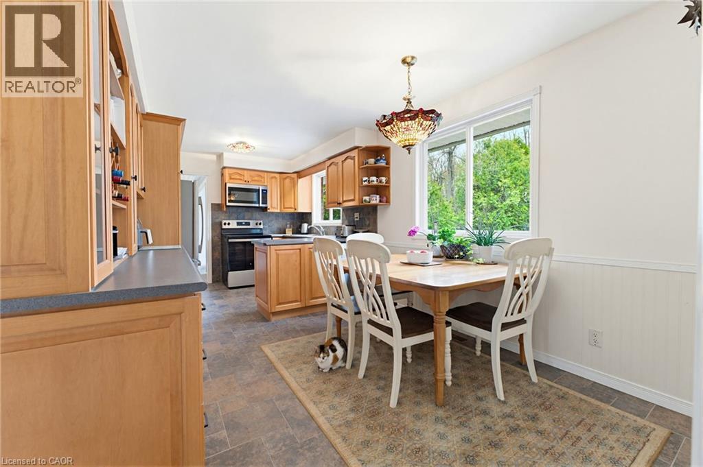Kitchen featuring light wood cabinetry with glass-front accents, dark countertops, and stainless steel appliances including a microwave and range - 10 Huisman Lane, Hamilton, ON