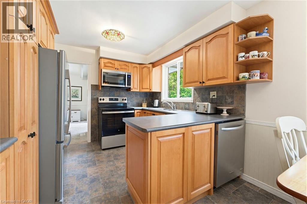 Kitchen featuring light wood cabinetry, stainless steel appliances, dark countertop surfaces, and a tiled backsplash - 10 Huisman Lane, Hamilton, ON