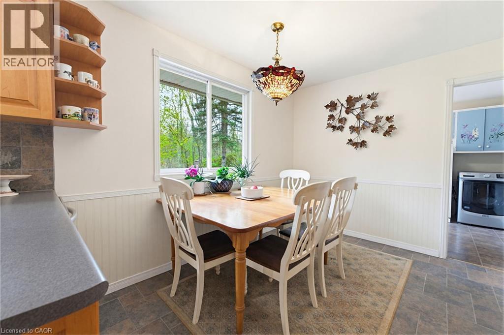 Dining area featuring a window overlooking greenery, wood-finish flooring, wainscoting, and a decorative overhead light fixture - 10 Huisman Lane, Hamilton, ON