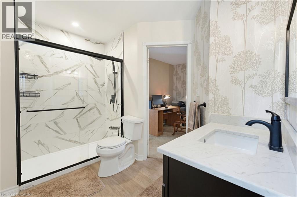 Ensuite Bathroom featuring a shower with a sliding glass enclosure, white marble-look wall tiles, and black fixtures - 10 Huisman Lane, Hamilton, ON
