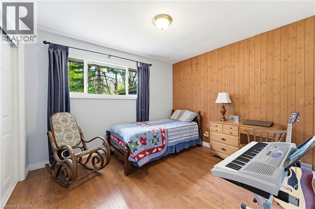Bedroom featuring wood-finish flooring, a paneled accent wall, light gray painted walls, a flush-mount ceiling light, and a window with exterior views - 10 Huisman Lane, Hamilton, ON