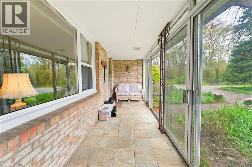 Enclosed porch featuring a brick half-wall, large windows, sliding glass doors, and tiled flooring - 10 Huisman Lane, Hamilton, ON