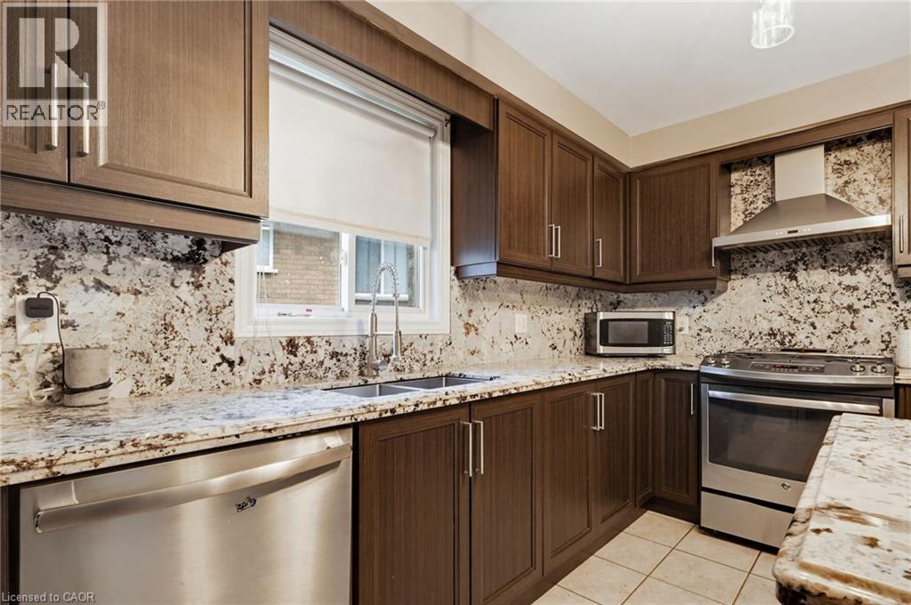 Kitchen featuring wood-finish cabinetry, patterned stone countertops, stainless steel appliances, and a window above the sink - 47 Hannah Crescent, Hamilton, ON - Indoor Photo Showing Kitchen With Double Sink