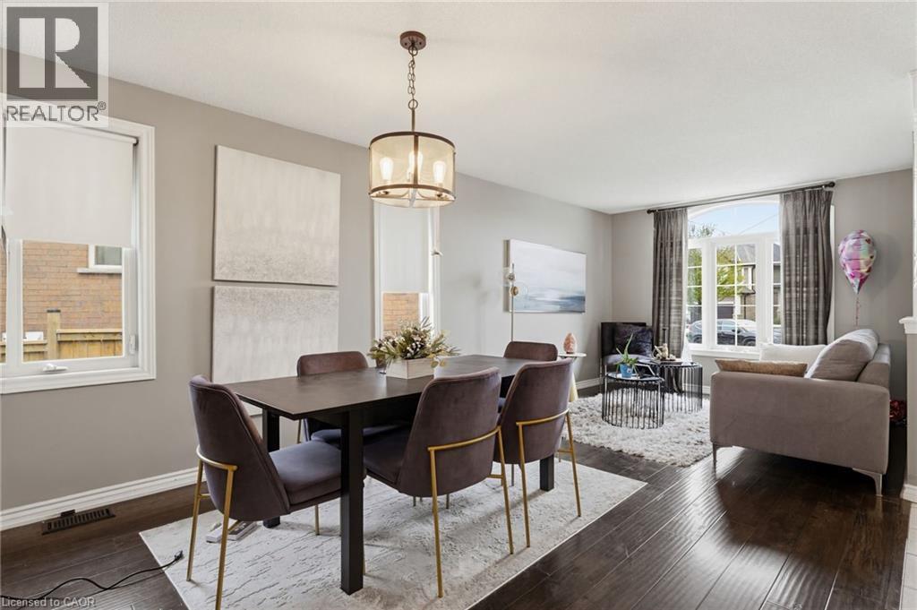 Open-concept living space featuring wood-finish flooring, a contemporary chandelier, large windows with roller shades, and neutral wall tones - 47 Hannah Crescent, Hamilton, ON - Indoor
