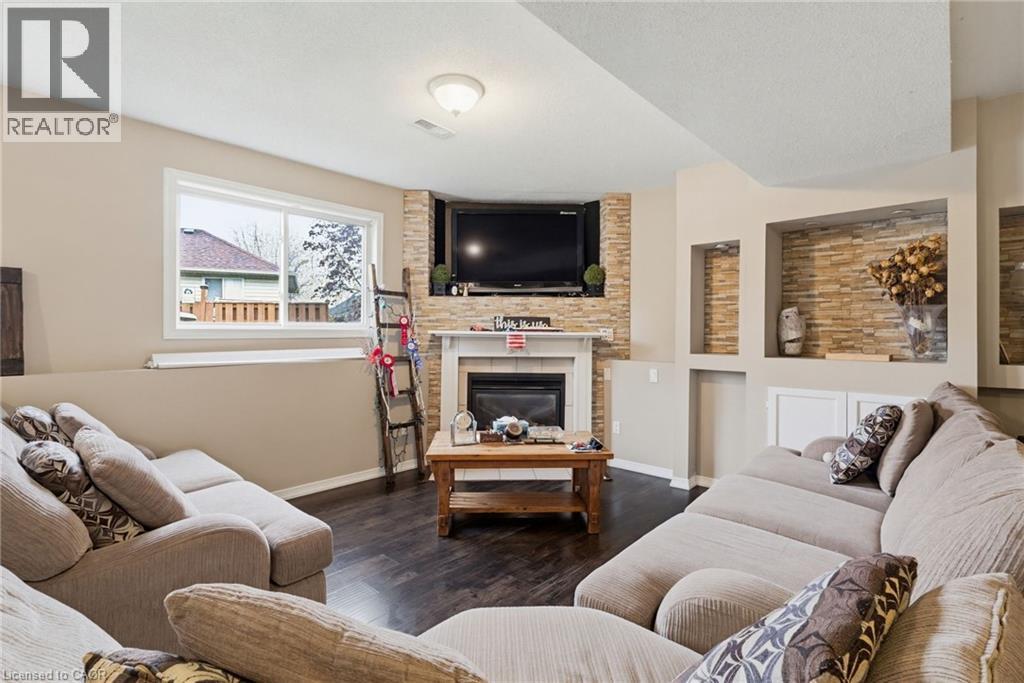 Living space featuring wood-finish flooring, a corner fireplace with a stone surround and mantle, a large window, and built-in shelving with stone accents - 47 Hannah Crescent, Hamilton, ON - Indoor Photo Showing Living Room With Fireplace