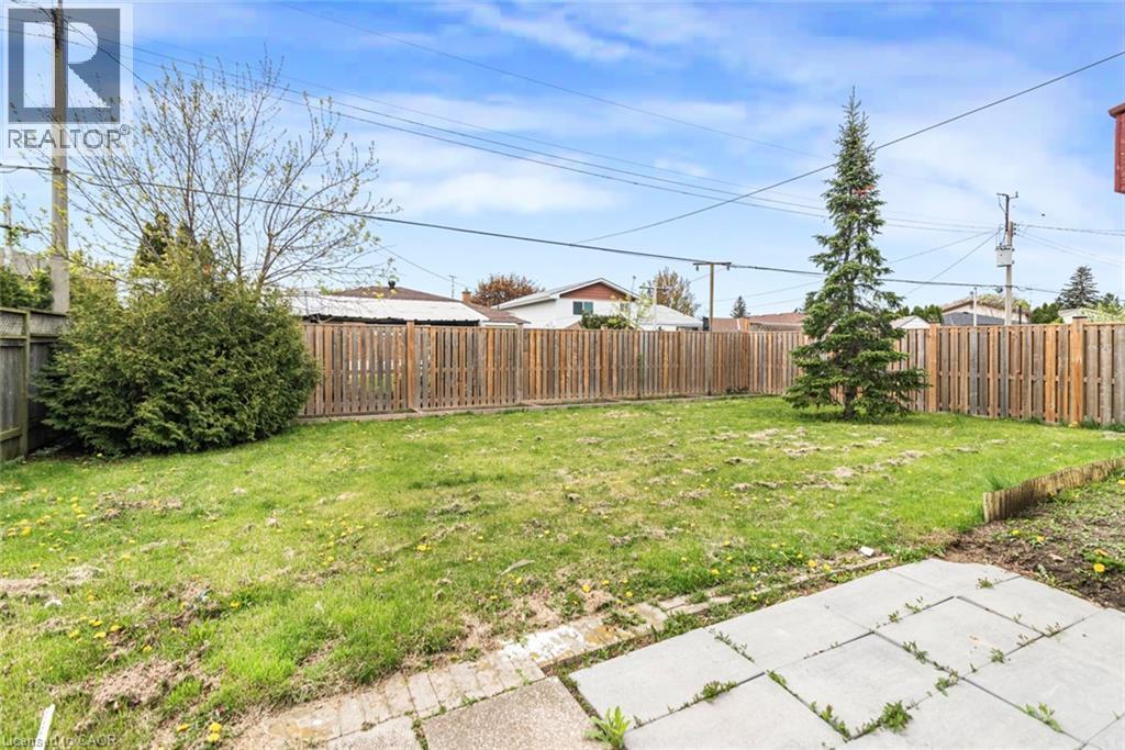Expansive backyard featuring a large grass area, wood fencing, mature evergreen tree, and a concrete patio - 112 Nash Road S, Hamilton, ON - Outdoor