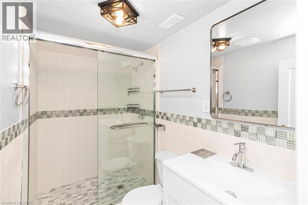 Bathroom featuring a glass-enclosed shower with mosaic tile flooring and a decorative tile accent band - 112 Nash Road S, Hamilton, ON - Indoor Photo Showing Bathroom