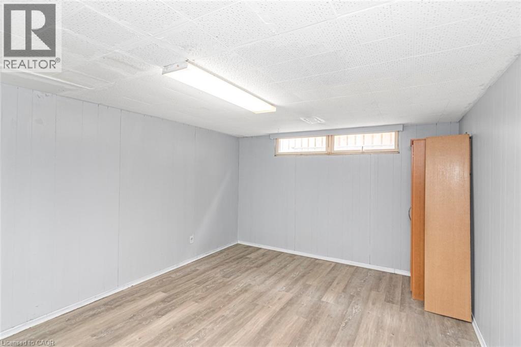 Spacious room featuring light wood-finish flooring, light grey paneled walls, and a white acoustical tile ceiling with a fluorescent light fixture - 112 Nash Road S, Hamilton, ON - Indoor